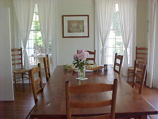 an old dining room table set up with matching chairs and a vase of flowers