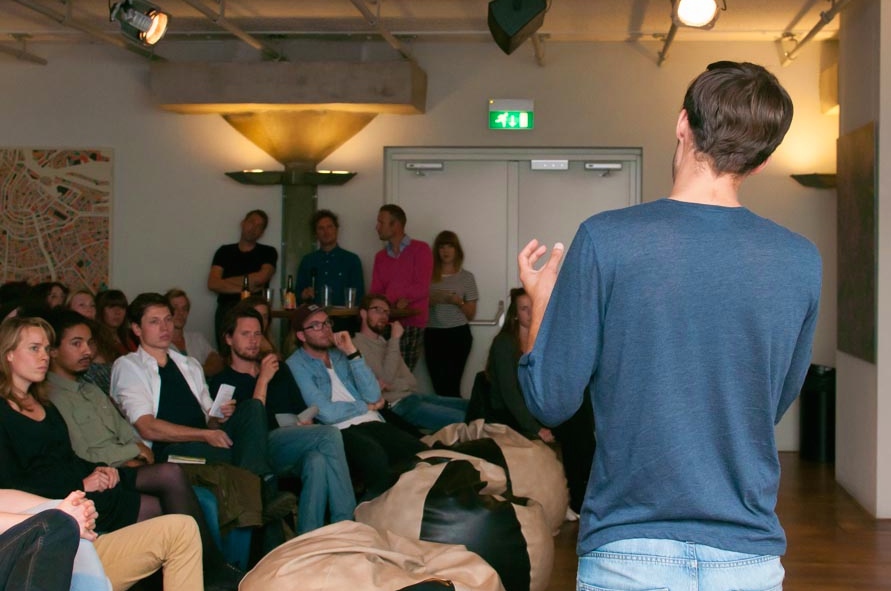 a man in blue shirt and jeans speaking to a large group