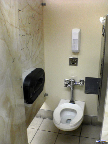 a toilet stall with graffiti on the wall and a roll of toilet paper
