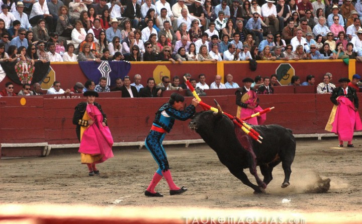 a man holding the tail of a black bull while people watch from a stadium