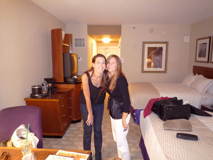 two women are smiling and standing beside a large bed