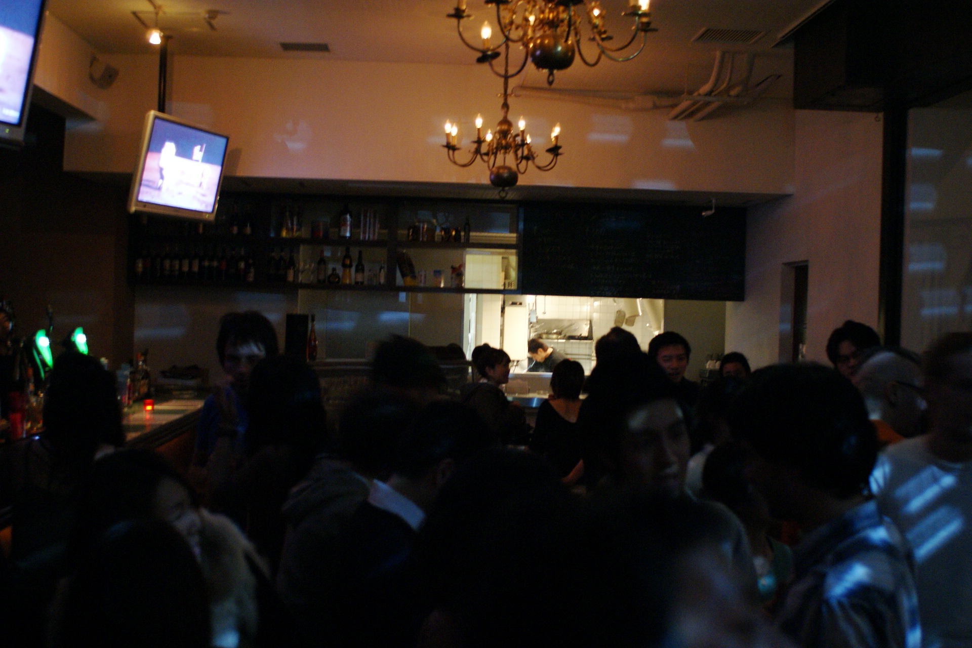 a large group of people stand in front of a bar with drinks and televisions