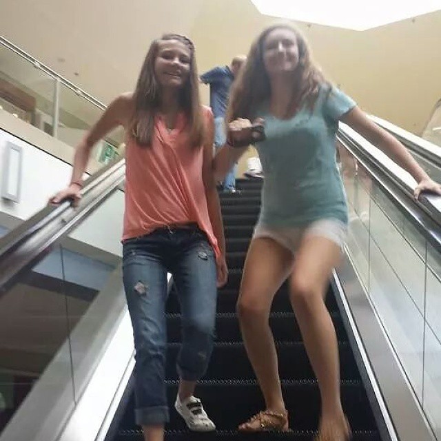 two girls riding down an escalator holding hands