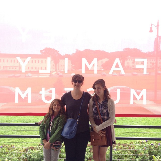 three women pose in front of a sign for a museum