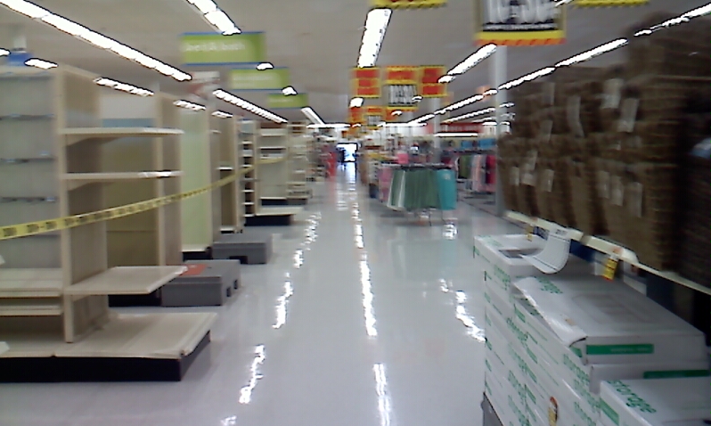 an empty store aisle full of boxes with signs hanging above