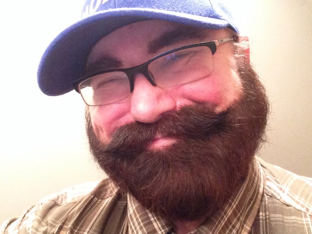 a bearded man with glasses and a cap is taking a selfie