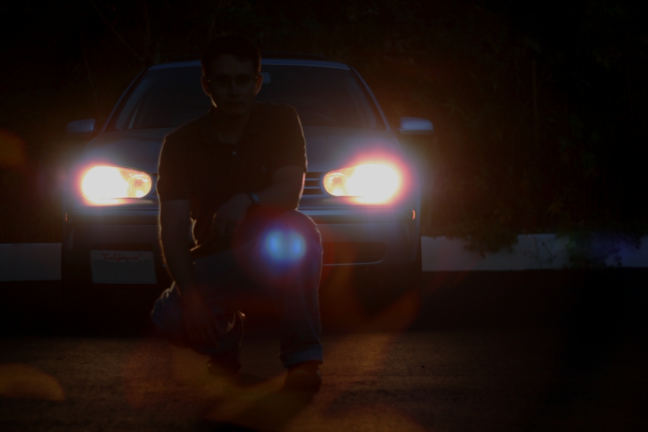 a man sitting on a bench in the dark beside a car