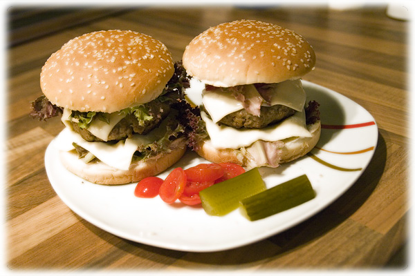 two hamburgers sitting on top of a white plate with pickles and tomato slices