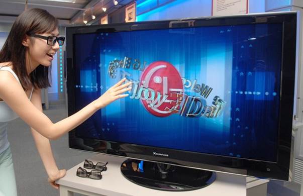 the lady is standing near the television and pointing at it