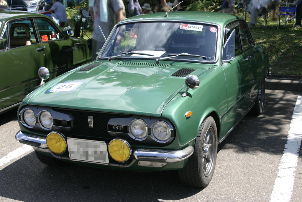 an old green car parked in a parking lot with other cars