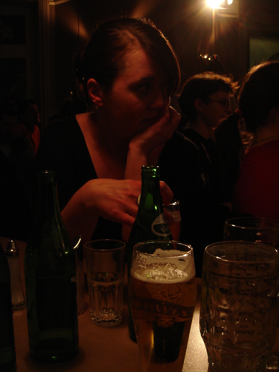 a girl is sitting at a table with two glasses and a beer bottle