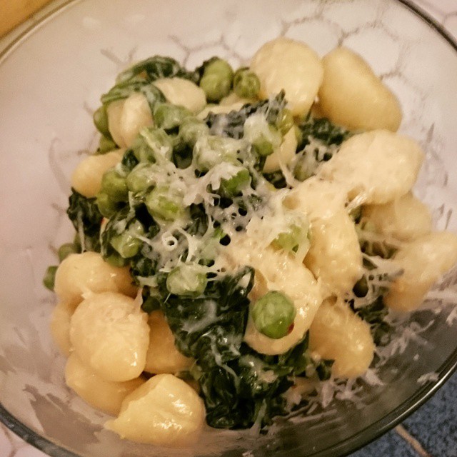 a bowl containing some ravioli, green peas, and cheese