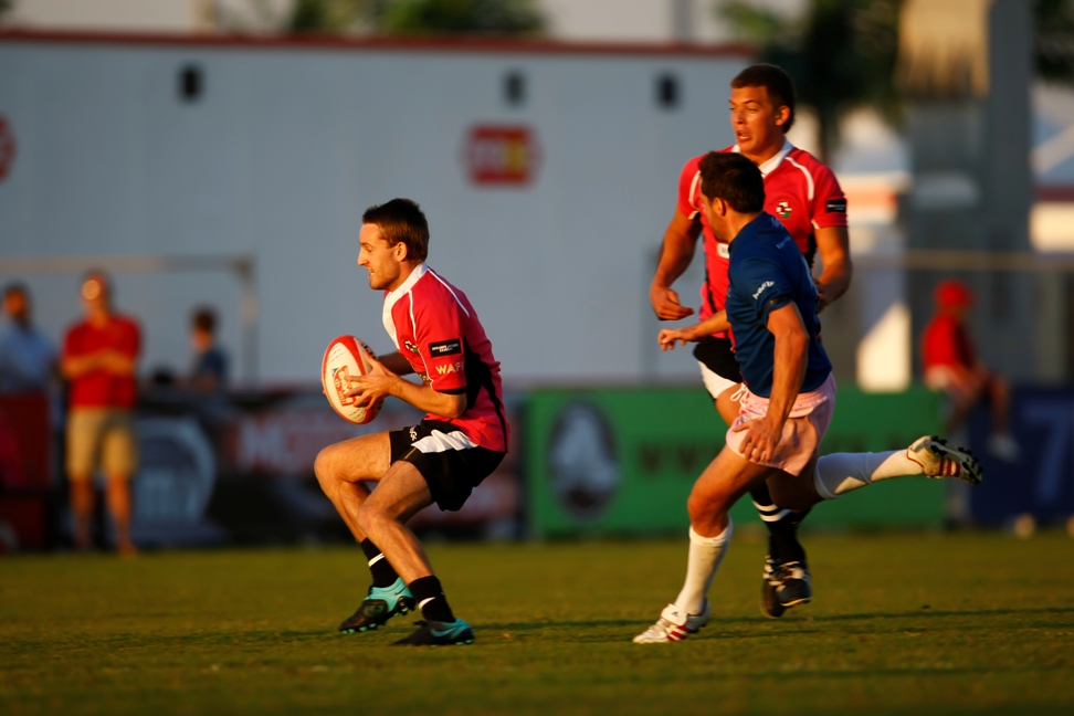 two men wearing red and blue are running with a white ball