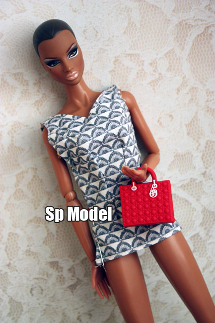 doll sitting next to a fake hand holding a red purse