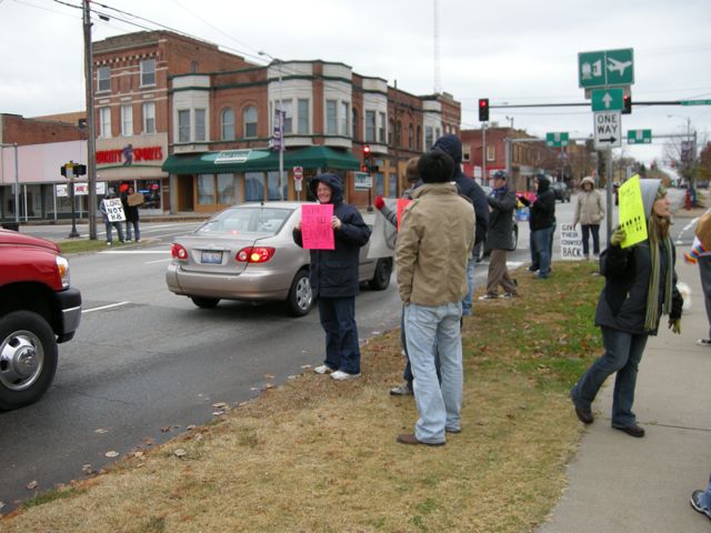 a group of people standing on the corner in front of a parked car