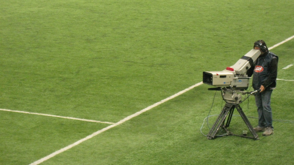a man in a field is holding a video camera and standing next to a television set