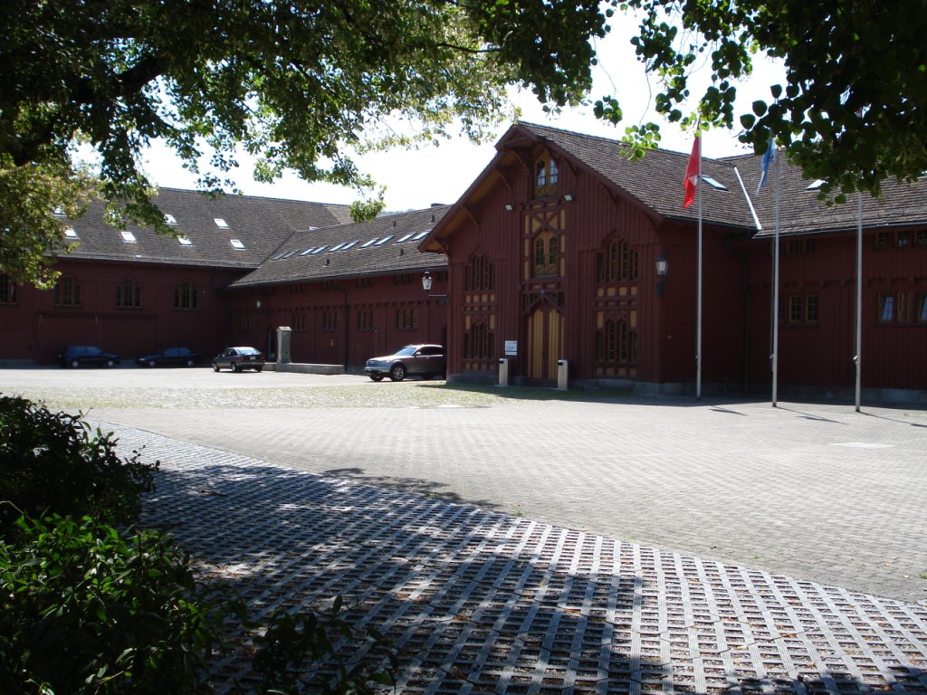 a red building with three rows of trees near by