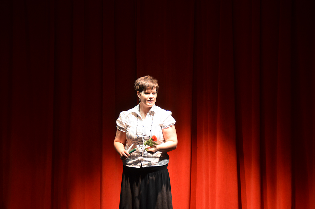 the woman is standing on a stage while holding her red rose