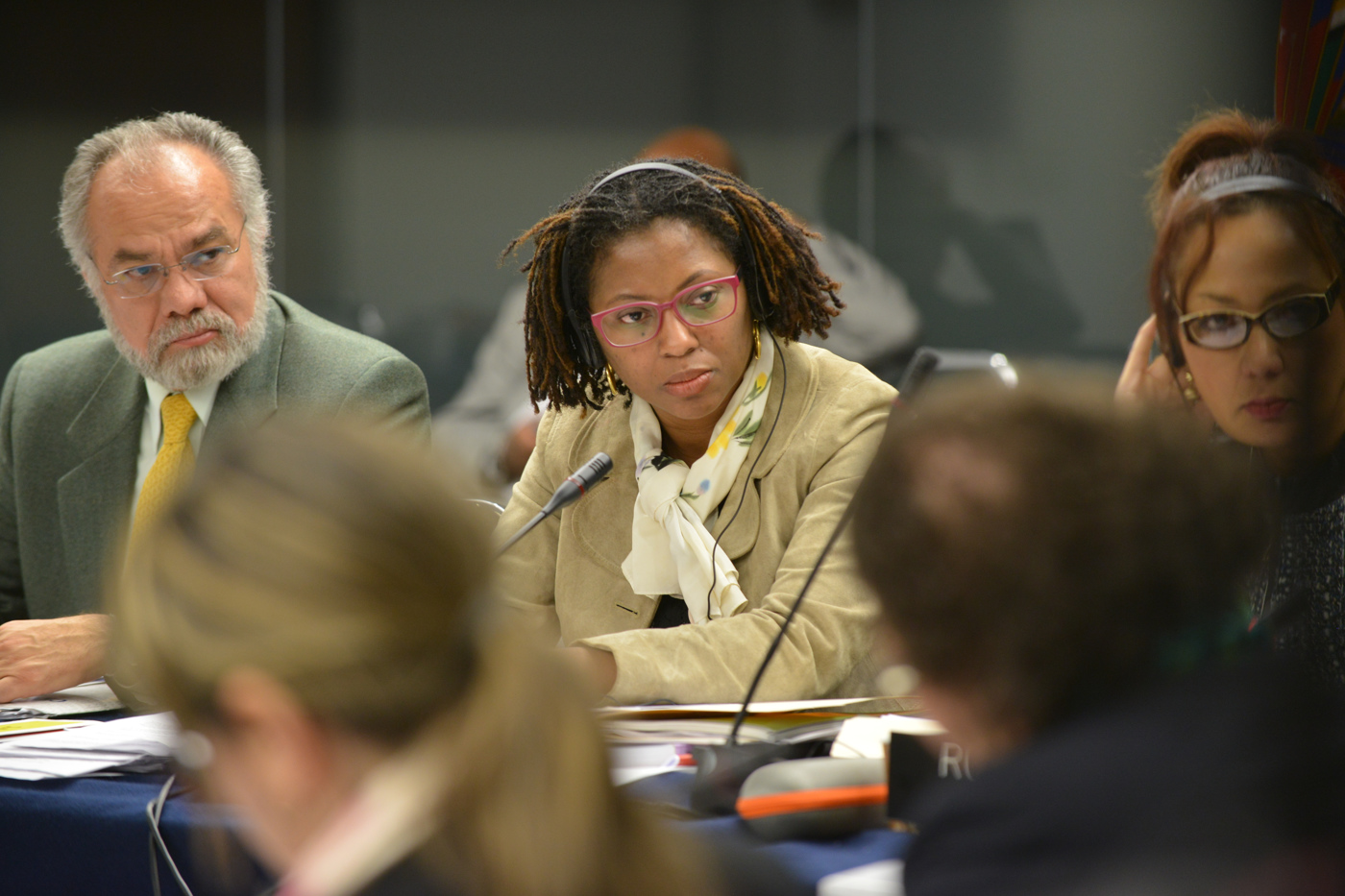 three people in a room at a table, and one is listening to the speaker