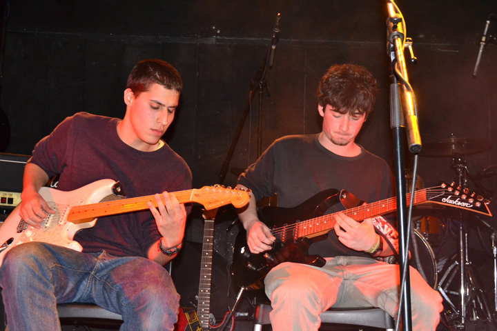a couple of young men sitting on a stage with guitars