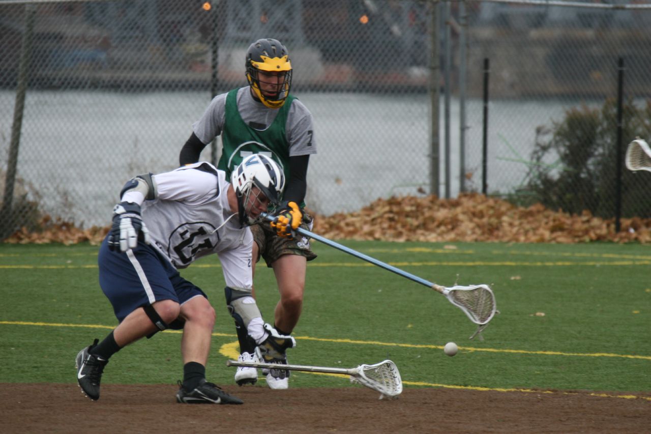 two young men play a game of lacrosse on an urban field