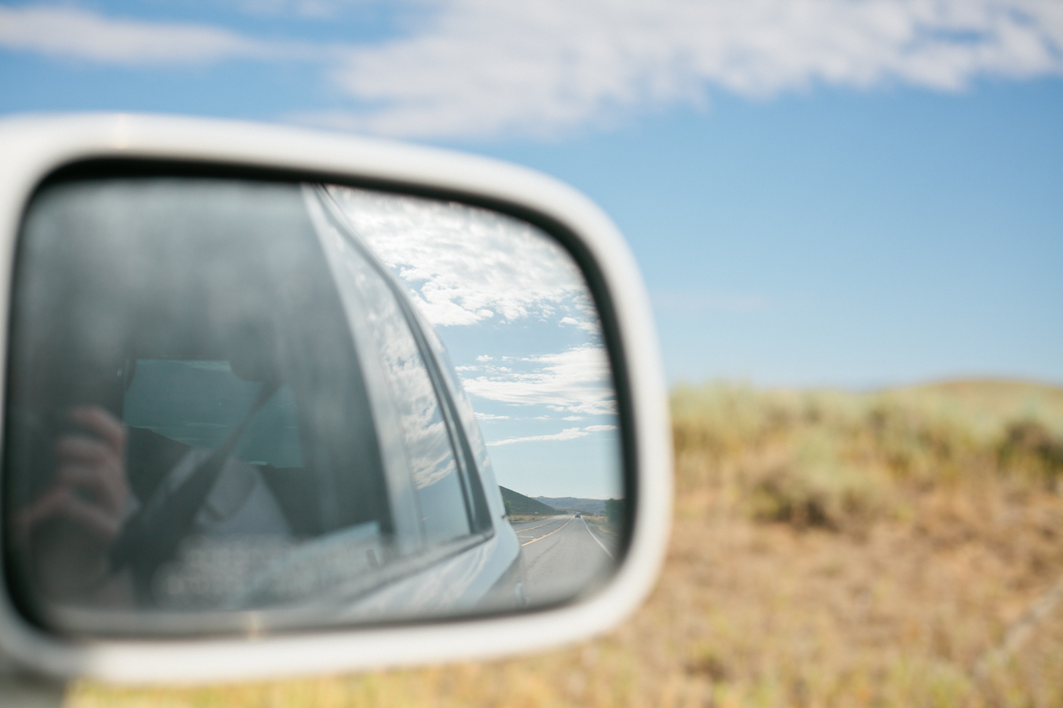 a reflection in a car's rear mirror of a road with the driver in the background