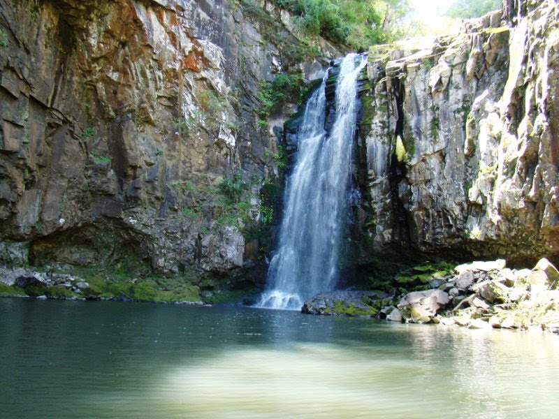 a waterfall at the top of a cliff next to a body of water