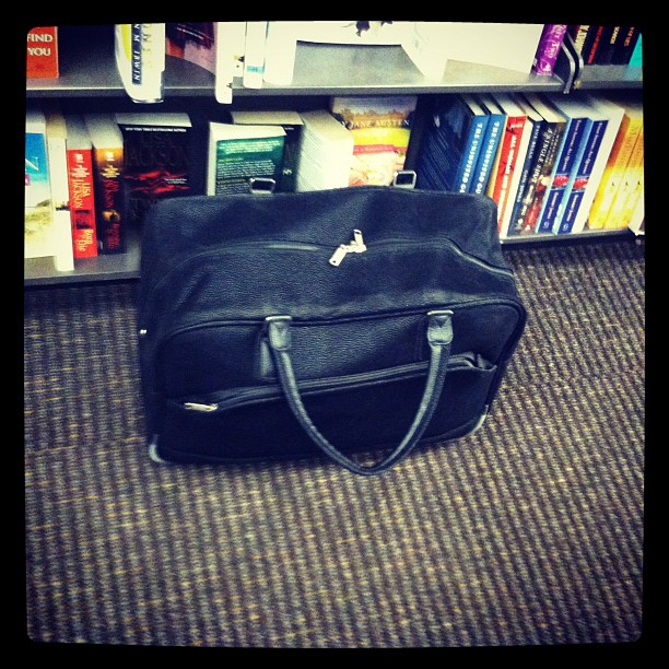 the black handbag sits on the carpet next to bookshelves