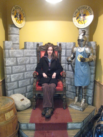 a lady sits in a knight like chair with other items on a red platform