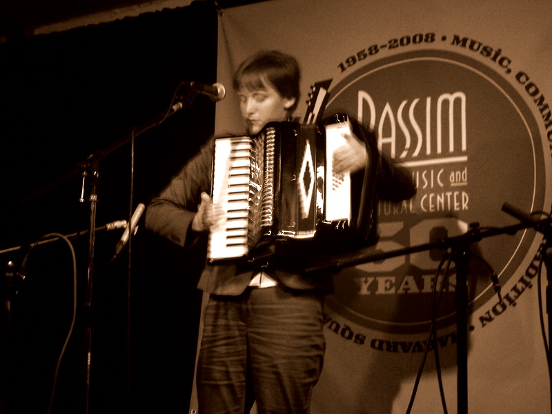 a man standing at a microphone holding a small accordion