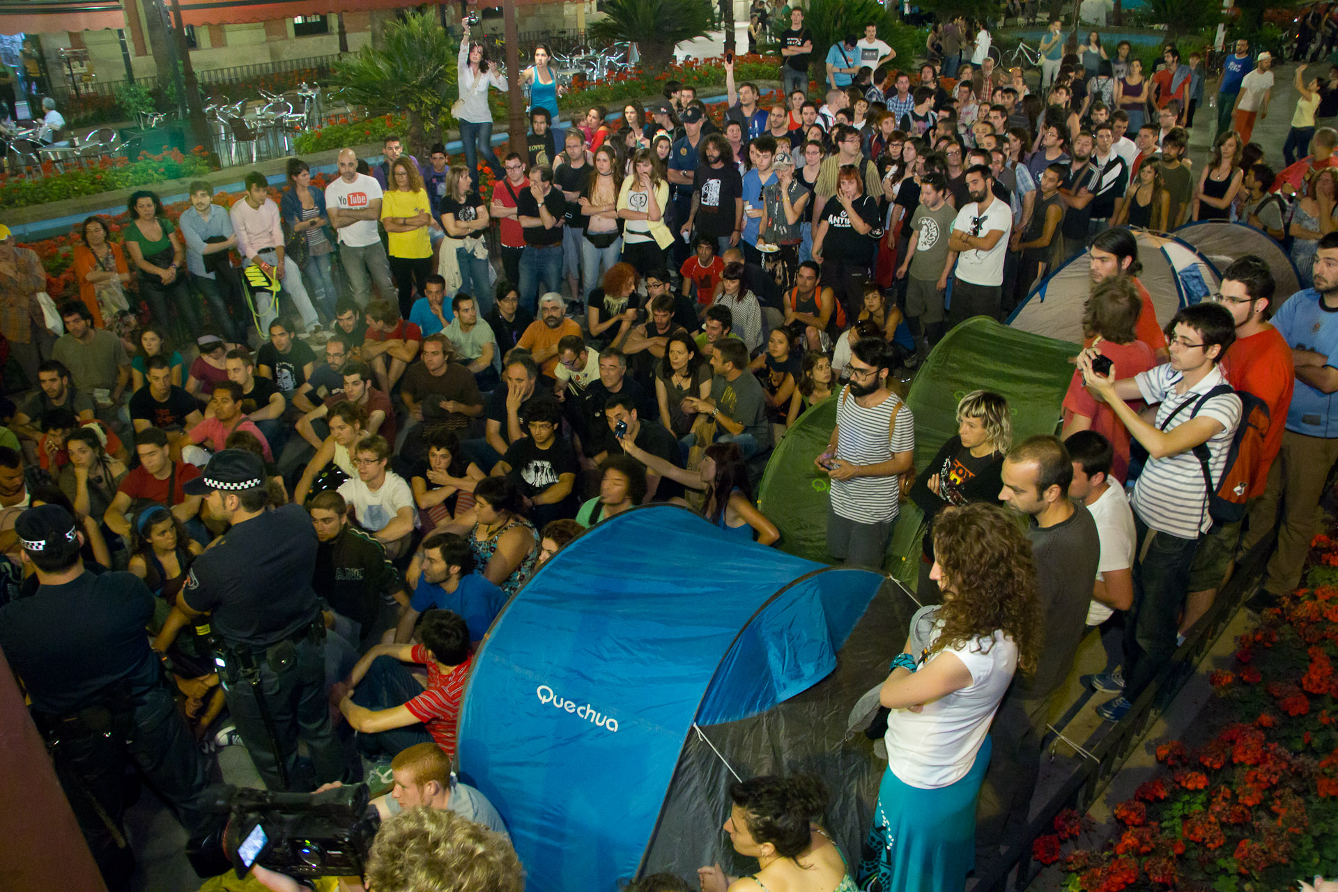 an outdoor concert crowd gathers around two people with tents in the air