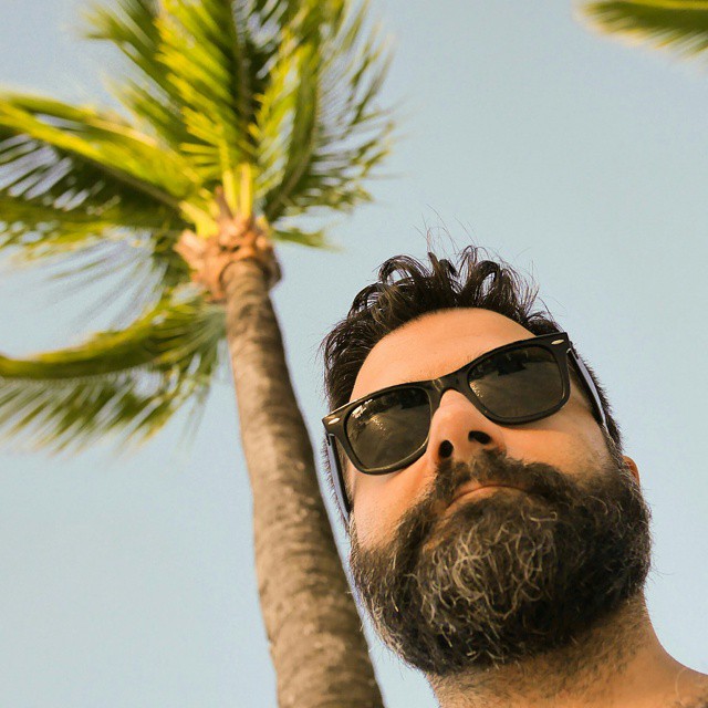 a man wearing sunglasses, standing in front of a palm tree