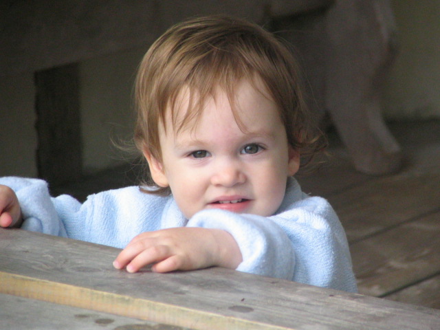 a young child with red hair is looking around the edge of a wooden bench