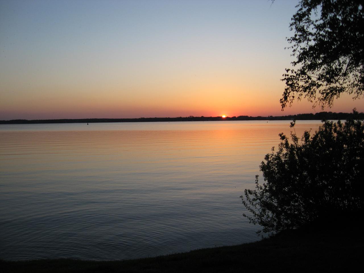 the sun is setting over the water near some trees