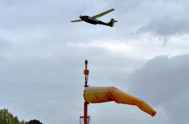 a plane flies in the sky over a wind tower