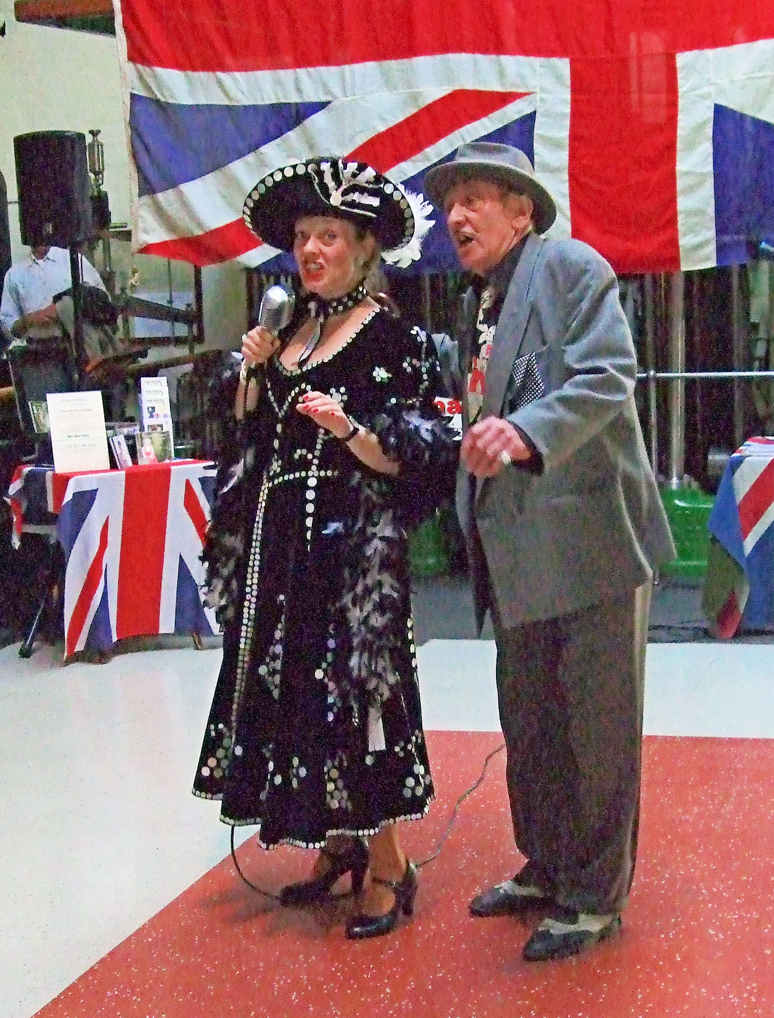 an older man standing next to an older woman wearing a black dress and hat