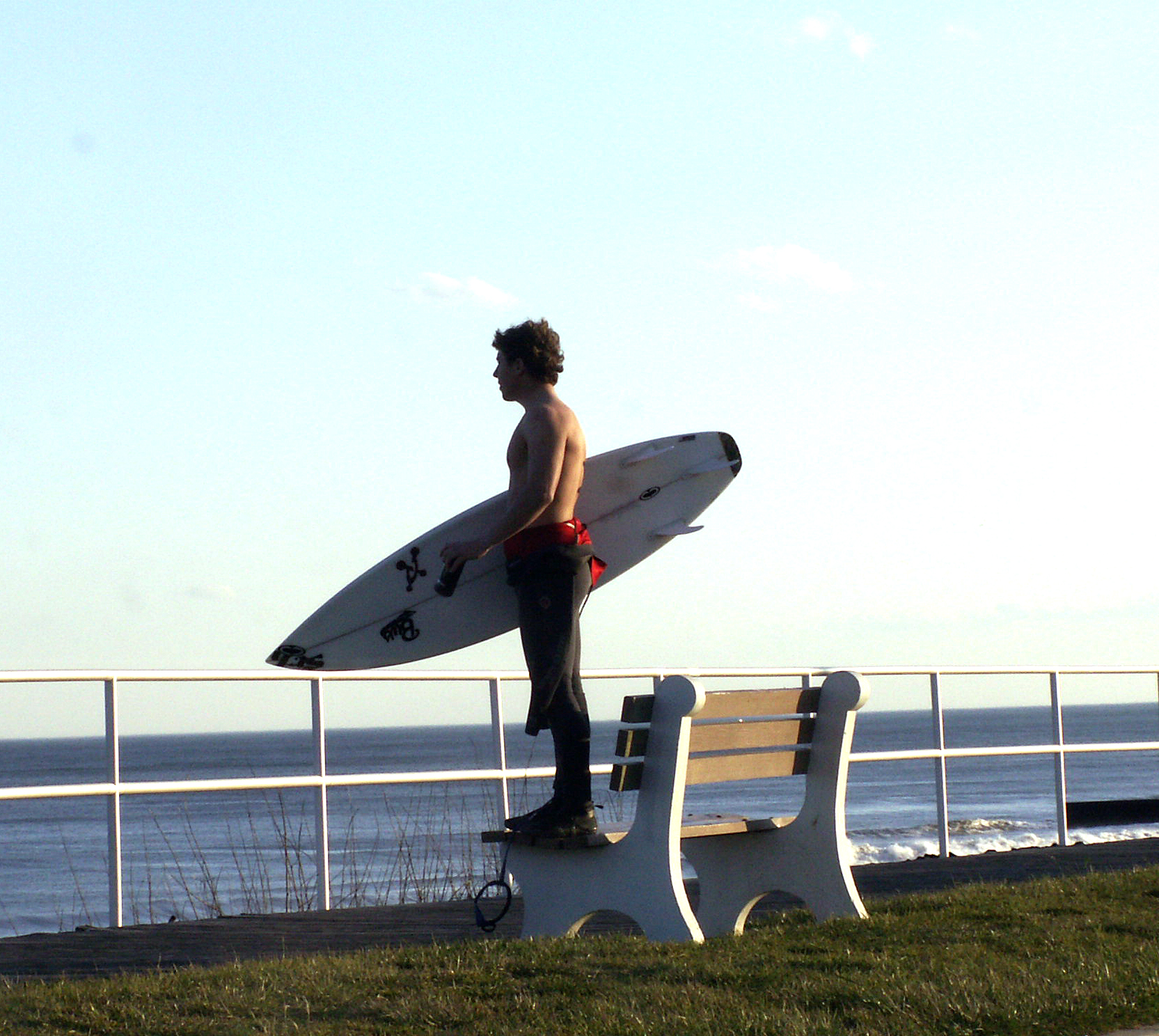 a man holding a surfboard on top of a wooden bench next to the ocean