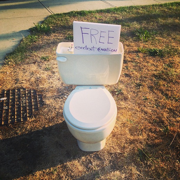 a toilet with a free sign attached to it sitting on the grass
