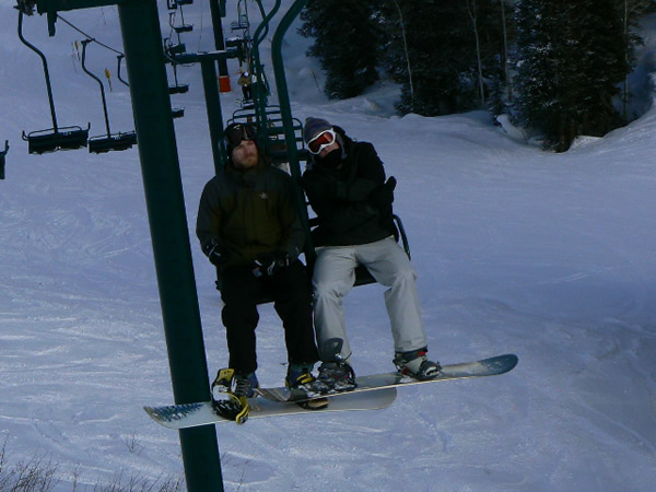 snowboarder in black with his friend hanging from a chairlift