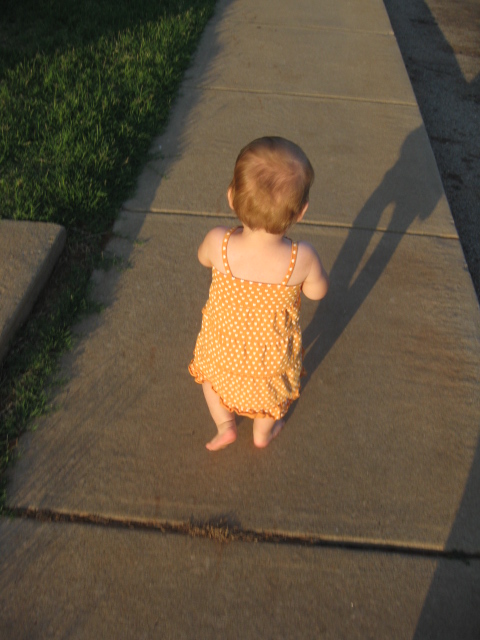 small child walking down the sidewalk near an adult