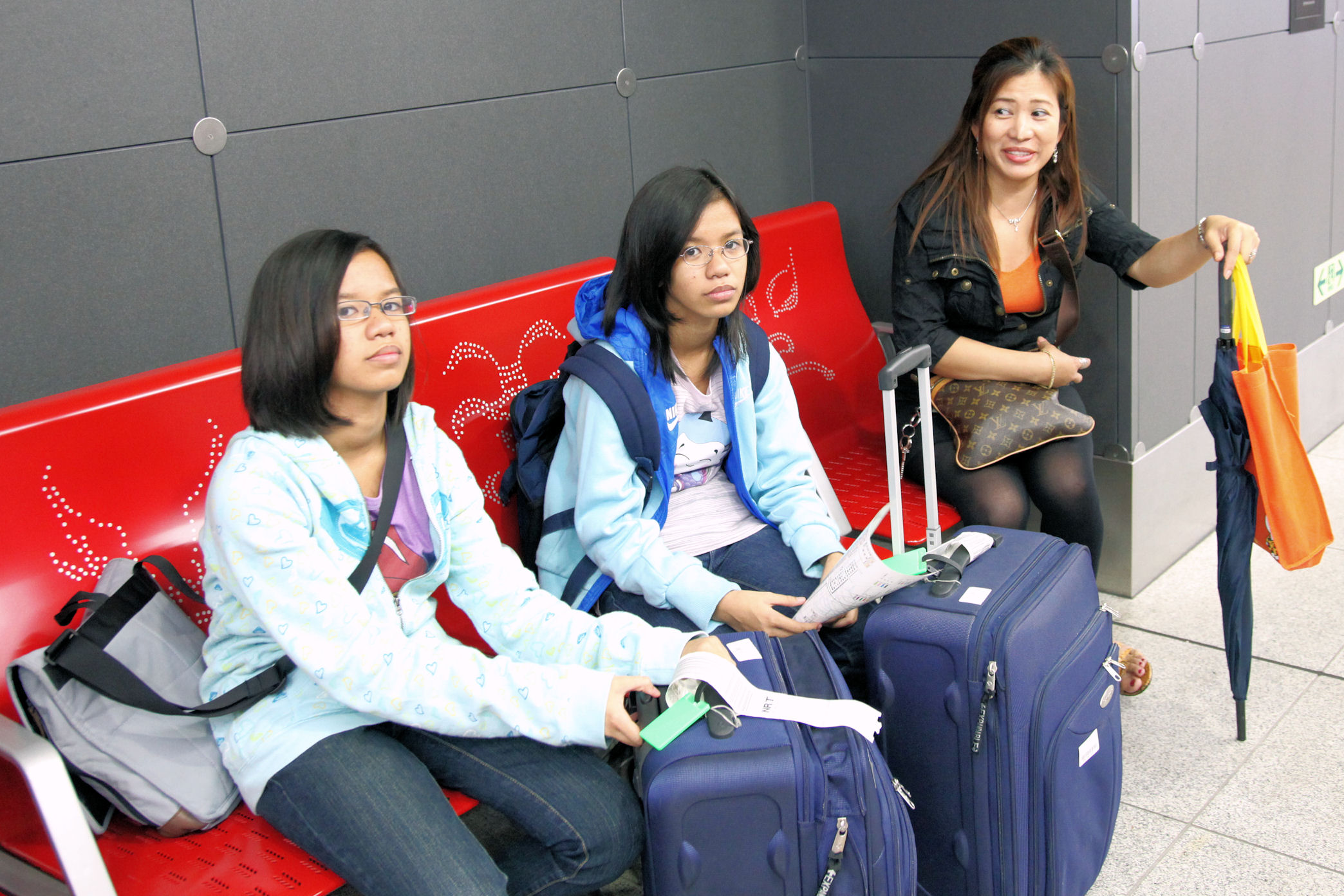 three asian women wait on a bench for luggage to pick up