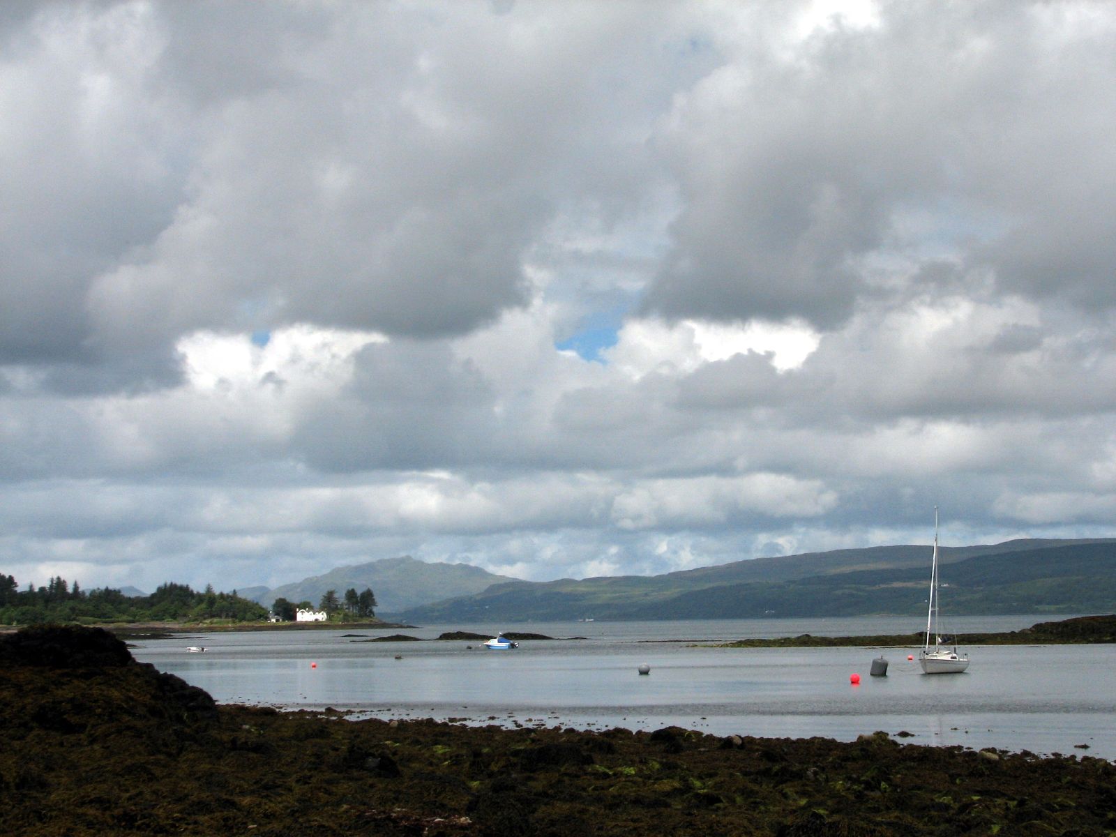 some sail boats in the water by a green hill