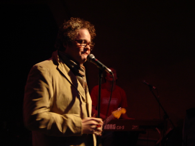 a man wearing glasses and a suit on stage speaking into microphone