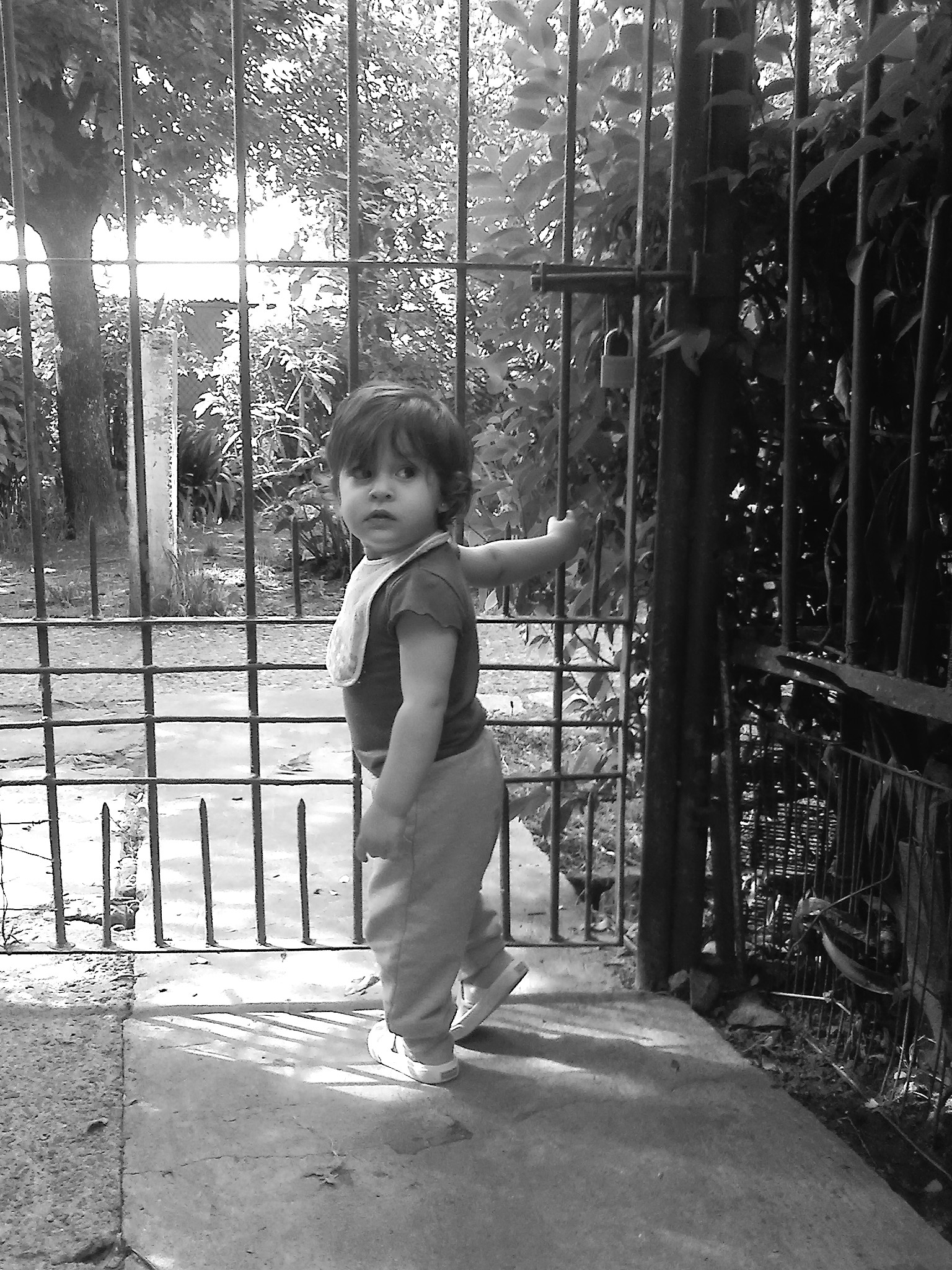 young child wearing sandals walking on walkway near iron fence
