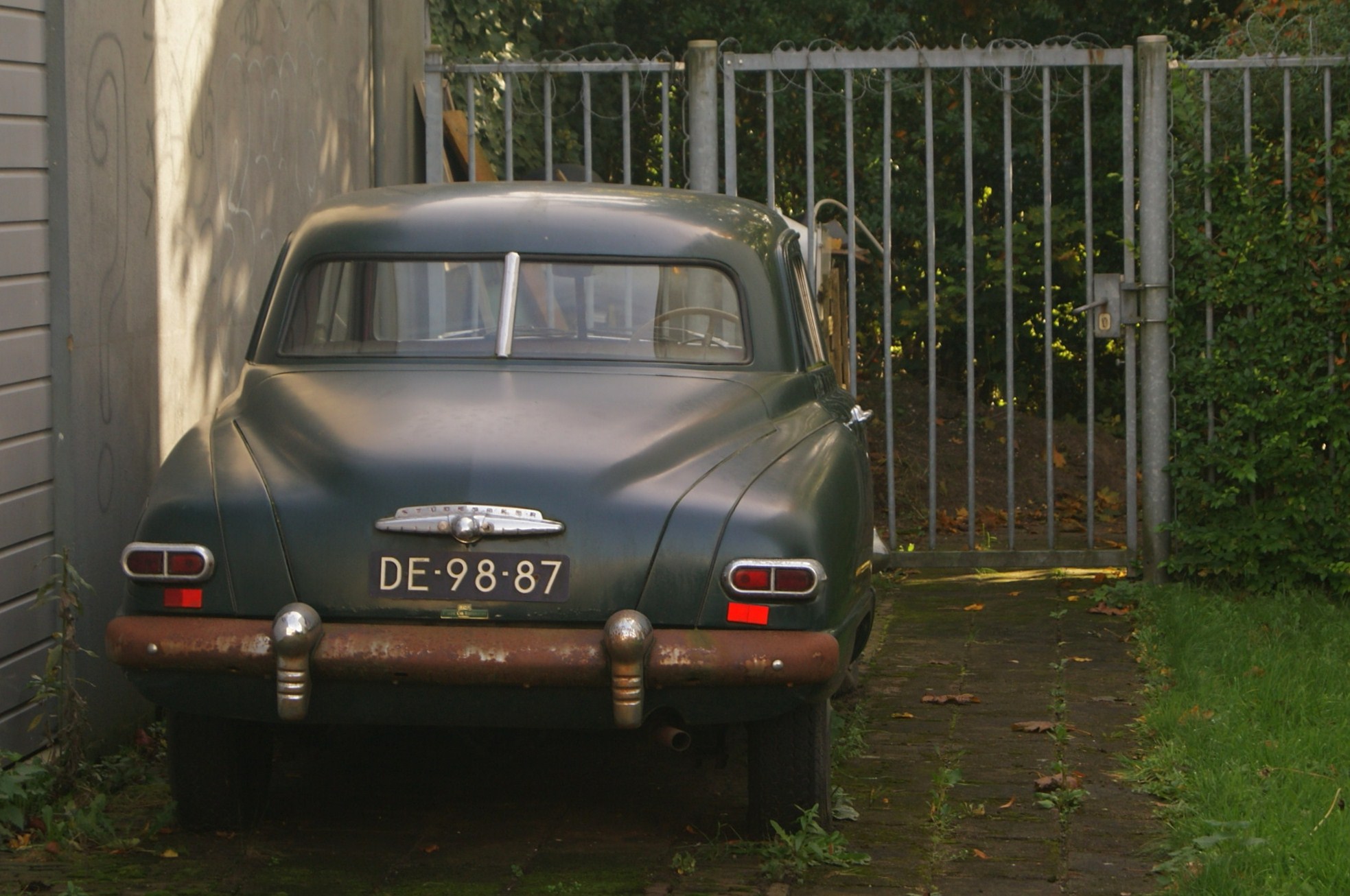 an old car sits parked behind a building in a driveway