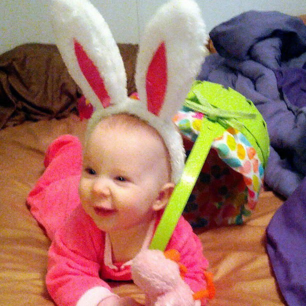 baby sitting on the bed wearing rabbit ears