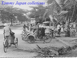 the old picture shows an asian street with people riding cars