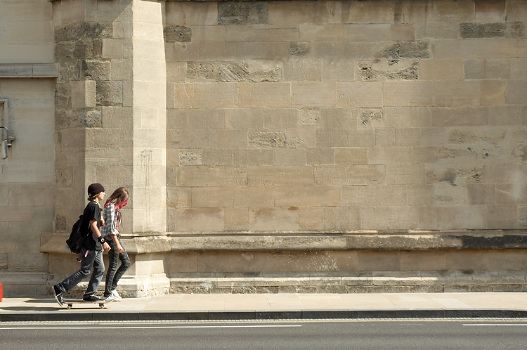 two people walk on a sidewalk next to a wall