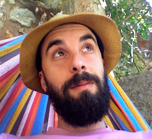man with beard wearing hat sitting in colorful hammock