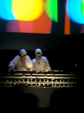 three people in white uniforms wearing yellow on top of a black box